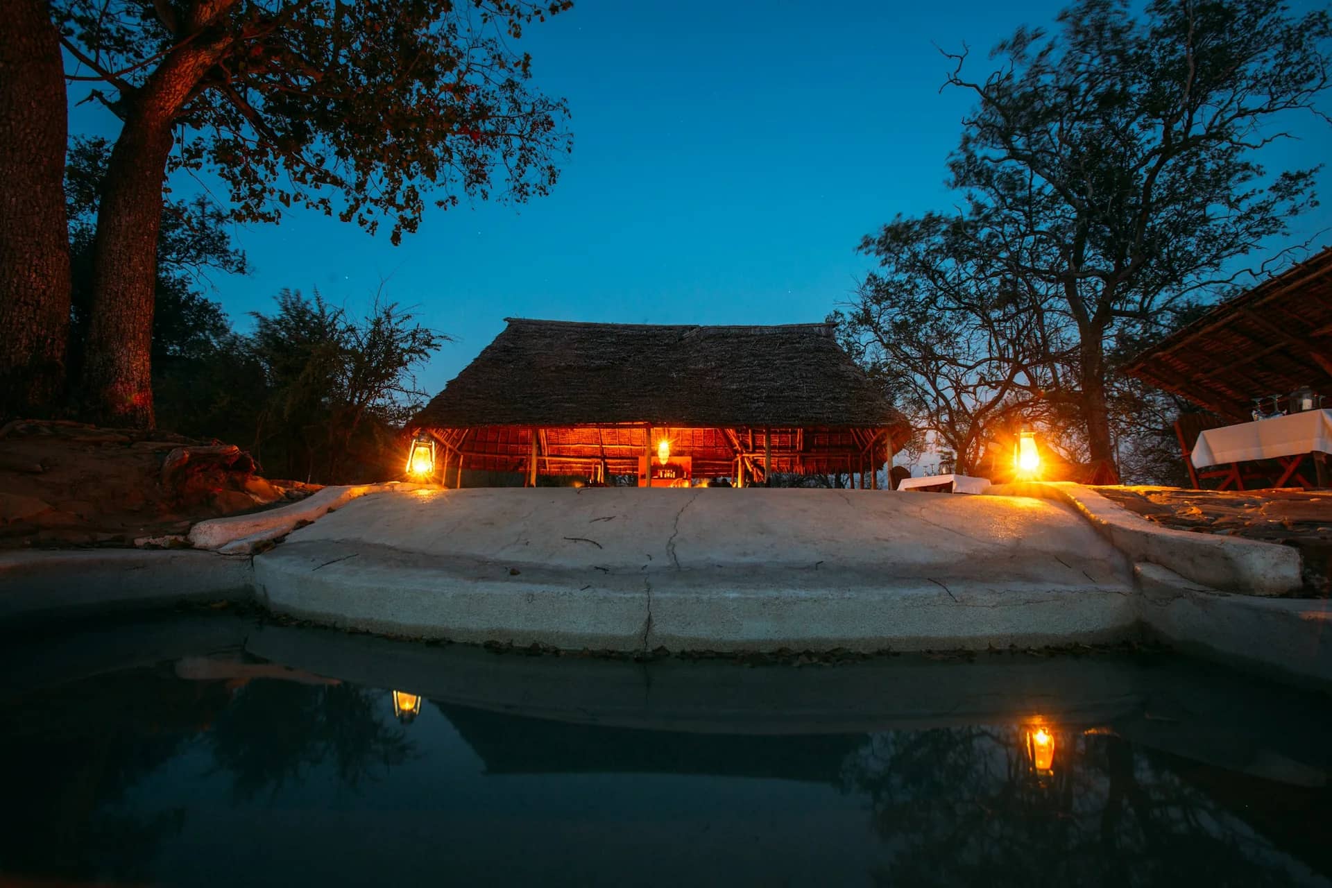 Thatched safari lodge and pool illuminated at dusk